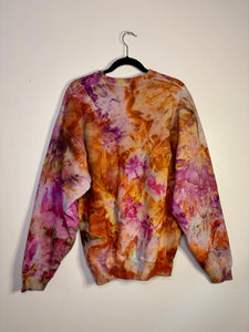 Hand-dyed vintage sweatshirt with a unique ice dye pattern in warm tones of orange, pink, and brown. Features a crewneck, long sleeves, and ribbed cuffs. Displayed on a black hanger against a white background.