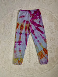 Vintage ice-dyed sweatpants featuring a mix of vibrant magenta, orange, and yellow hues against a light gray base. The pattern radiates outward, creating a bold and unique design. The pants have an elastic waistband and cuffs.