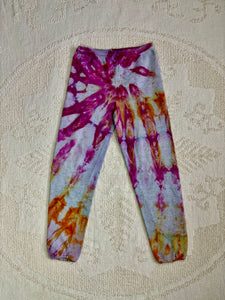 Vintage ice-dyed sweatpants featuring a mix of vibrant magenta, orange, and yellow hues against a light gray base. The pattern radiates outward, creating a bold and unique design. The pants have an elastic waistband and cuffs.